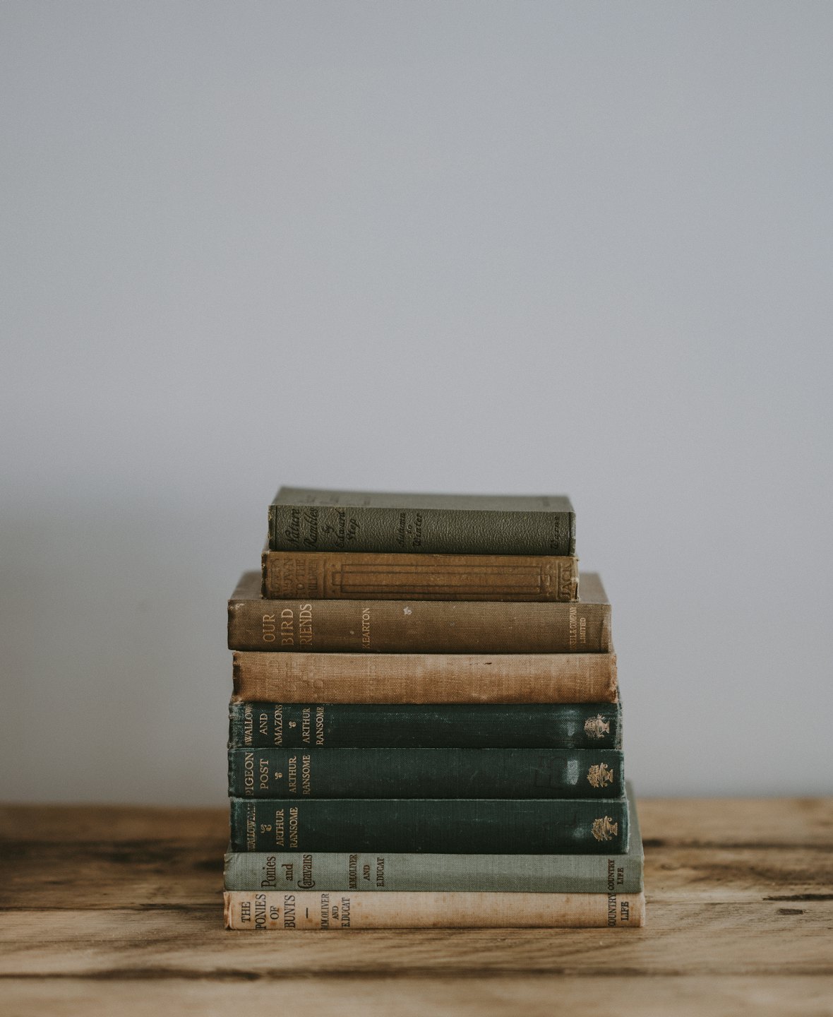 Stacked antique books with faded green and brown covers on a wooden table.